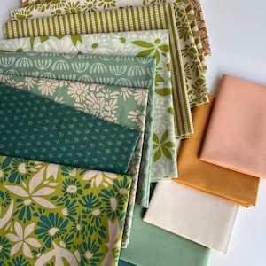 May include: A stack of fabric squares in various shades of green, brown, and white with floral and geometric patterns. The fabric squares are arranged in a fan shape on a white surface.