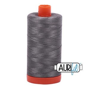 Puede incluir: Una bobina de hilo gris con tapa y base naranja. El hilo está enrollado firmemente alrededor de la bobina. La marca "AuriFil" está impresa en el lateral de la bobina en blanco y azul.