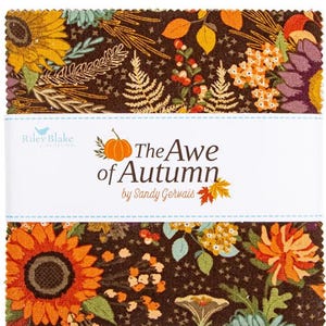 Op de afbeelding: Een stapel stoffen vierkanten met een herfstthema bloemenpatroon. De stof heeft zonnebloemen, bladeren en andere herfst elementen in tinten oranje, geel en bruin. Het label luidt "The Awe of Autumn" van Sandy Gervais.