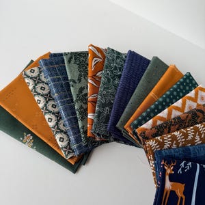 Peut inclure: Une collection de carrés de tissu pliés disposés en éventail, présentant divers motifs floraux, géométriques et forestiers dans des tons de vert foncé, bleu marine, jaune moutarde, orange brûlé et blanc.