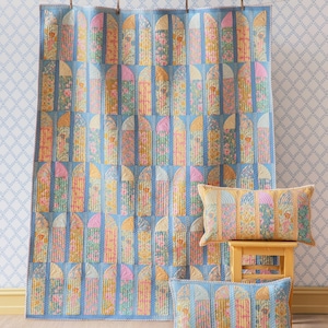 Könnte beinhalten: Eine blaue Steppdecke mit einem sich wiederholenden Muster aus bogenförmigen Fenstern in Rosa, Gelb und Grün. Zwei passende rechteckige Kissen befinden sich auf einem kleinen Holzschemel und auf dem Boden. Die Steppdecke hängt an einer Wäscheleine.