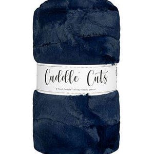 May include: A navy blue faux fur throw blanket with the text "Cuddle Cuts" on a white label.