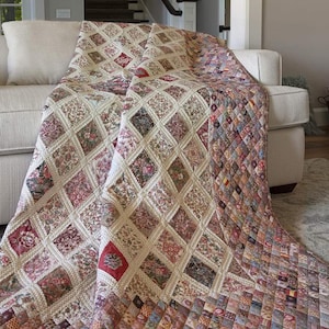 Może przedstawiać: Kołdra w kolorze beżowym i brązowym z wzorem rombów. Kołdra wykonana jest z różnych tkanin z kwiatowymi nadrukami. Jest ona zarzucona na beżową kanapę.