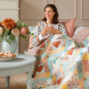 May include: A patchwork quilt featuring a variety of floral and gingham fabric squares in shades of blue, yellow, red, and white. The quilt is decorated with multiple heart-shaped appliqués, some of which contain small house illustrations.