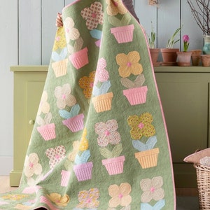 Pode incluir: Uma colcha verde com um padrão floral rosa, amarelo e azul. A colcha apresenta um desenho repetitivo de flores em vasos.