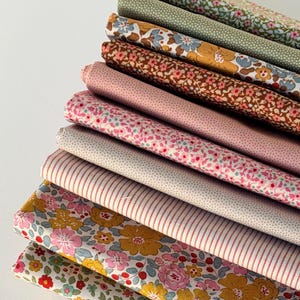 May include: A stack of ten folded fabric pieces featuring various patterns including small floral prints in shades of pink, yellow, blue, and green, a solid sage green texture, and a white fabric with thin vertical brown stripes.