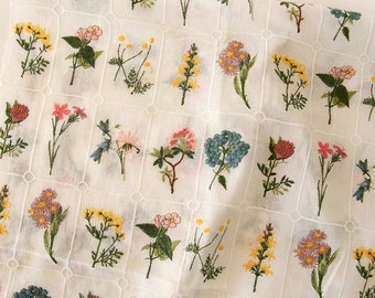 May include: White fabric with a grid pattern featuring embroidered floral designs in various colors, including pink, yellow, blue, and red.