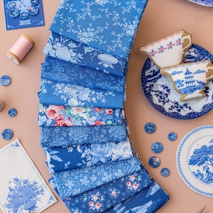 Puede incluir: Colección de telas azules con estampados florales, botones y elementos decorativos. La imagen incluye carretes de hilo, una figura de pájaro y tijeras. Las telas presentan diversos diseños florales, incluyendo rosas. Los elementos están dispuestos sobre una superficie.
