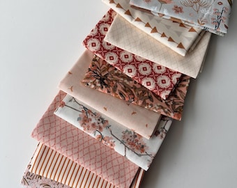 May include: A stack of eight folded fabric squares featuring various patterns including a deer and floral print, geometric shapes, stripes, and botanical motifs in a color palette of soft pink, cream, terracotta, and muted grey tones.