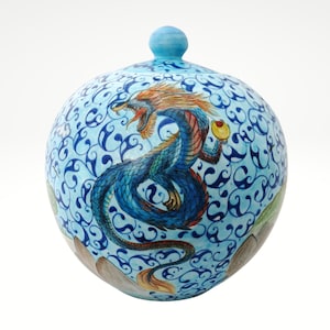 Op de afbeelding: Een blauwe keramische pot met een deksel, versierd met een handgeschilderde draak en wervelende patronen.