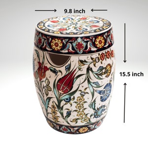 Può includere: Uno sgabello in ceramica con una base bianca e disegni floreali colorati. La parte superiore dello sgabello ha un design circolare con un centro blu e bianco. Lo sgabello misura 9,8 pollici di diametro e 15,5 pollici di altezza.
