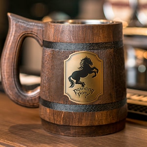 Op de afbeelding: Houten bierpul met een donkerbruine afwerking en een grote handgreep. De pul heeft een metalen binnenkant en een gouden embleem met een zwart paard en de woorden "Prancing Pony".