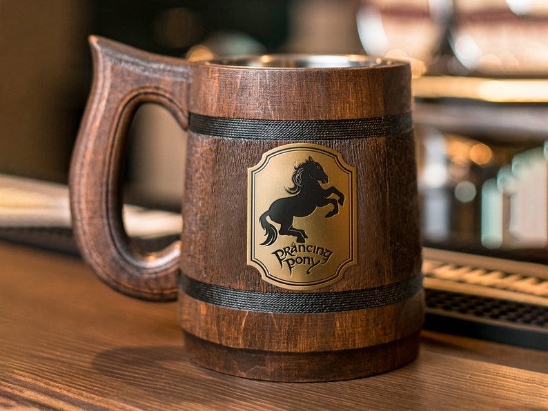 May include: Wooden beer mug with a dark brown finish and a large handle. The mug features a metal interior and a gold emblem with a black horse and the words "Prancing Pony".