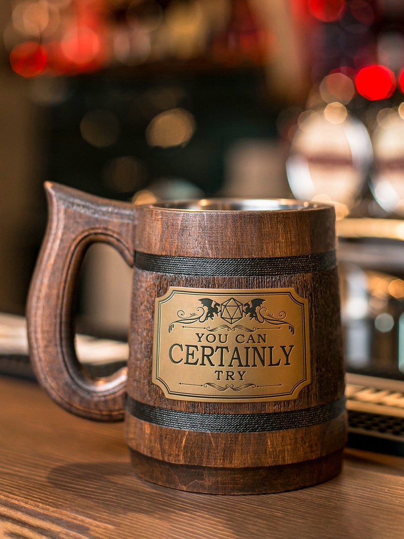 May include: A brown wooden beer stein with a black band around the top and bottom. The stein has a metal plate with the text "You can certainly try" and a stylized image of a 20-sided die.
