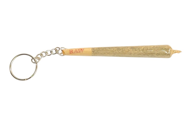 May include: A silver keychain with a realistic-looking, brown, rolled-up joint with a RAW label. The joint is attached to a silver chain and a silver ring.
