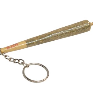 May include: A brown and green keychain shaped like a rolled joint with a silver chain and ring. The joint is labeled "RAW".