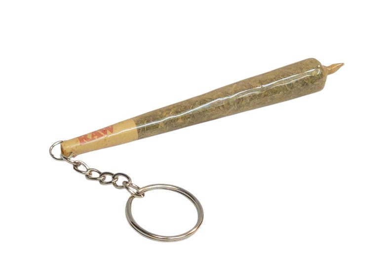 May include: A brown and green keychain shaped like a rolled joint with a silver chain and ring. The joint is labeled "RAW".