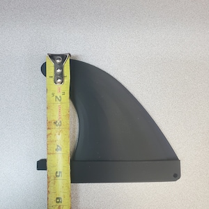 Pode incluir: Uma barbatana de prancha de surf preta com uma fita m&eacute;trica amarela ao lado. A barbatana tem aproximadamente 15 cm de altura. A fita m&eacute;trica &eacute; marcada em polegadas e p&eacute;s.