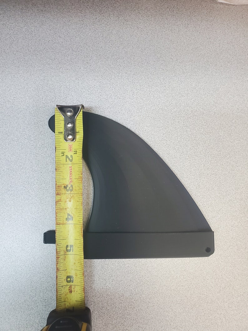 Pode incluir: Uma barbatana de prancha de surf preta com uma fita m&eacute;trica amarela ao lado. A barbatana tem aproximadamente 15 cm de altura. A fita m&eacute;trica &eacute; marcada em polegadas e p&eacute;s.