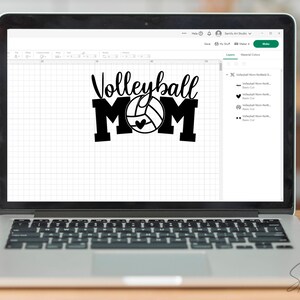 May include: A laptop screen shows a black and white graphic saying "Volleyball MOM" with a volleyball and heart design. The laptop is open on a wooden surface, with a blurred background.