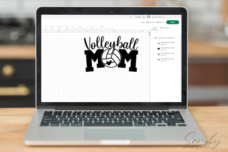 May include: A laptop screen shows a black and white graphic saying "Volleyball MOM" with a volleyball and heart design. The laptop is open on a wooden surface, with a blurred background.