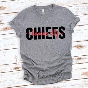 May include: A heather gray t-shirt with the word "CHIEFS" in large black letters, with "Kansas City" in red script underneath. The shirt is made of a soft material and has rolled-up sleeves.