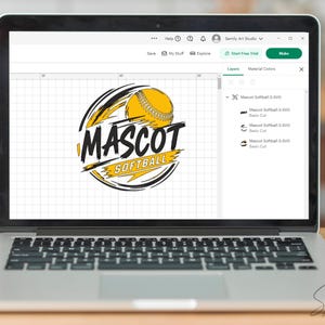 May include: Laptop displaying a softball logo design. The logo features a yellow softball with black and yellow accents, and the words "MASCOT SOFTBALL" in bold, stylized text. The laptop is on a wooden surface.