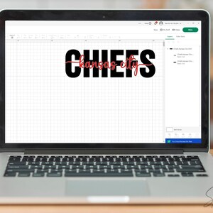 May include: A laptop displays the words "CHIEFS Kansas City" in a design program. The word "CHIEFS" is in bold black font, and "Kansas City" is in a cursive red font. The laptop is open on a wooden surface.
