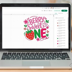 May include: A laptop screen displaying a digital graphic design with the text BERRY SWEET ONE in pink and green lettering, accompanied by a red strawberry illustration, small pink flowers, and red heart accents on a white grid background.
