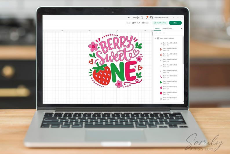 May include: A laptop screen displaying a digital graphic design with the text BERRY SWEET ONE in pink and green lettering, accompanied by a red strawberry illustration, small pink flowers, and red heart accents on a white grid background.