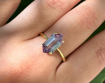 Puede incluir: Un anillo de oro con una piedra preciosa de color púrpura y verde de corte esmeralda.