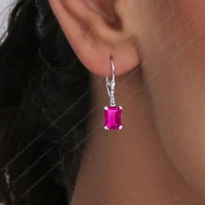 May include: A pair of silver earrings featuring a square pink gemstone. The earrings have a simple design and are suitable for everyday wear.