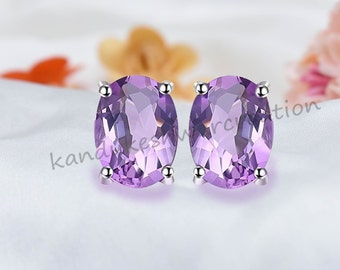 May include: A pair of silver stud earrings with oval-shaped amethyst gemstones. The gemstones are a light purple color.