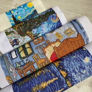 Op de afbeelding: Vier opgerolde stukken Aida-doek met kruissteekborduursels van beroemde schilderijen. Het bovenste stuk is een blauwe en gele sterrenhemel-sc&egrave;ne, het tweede is een blauw en groen landschap, het derde is een bruine en blauwe slaapkamer-sc&egrave;ne en het onderste is een andere blauwe en gele sterrenhemel-sc&egrave;ne.