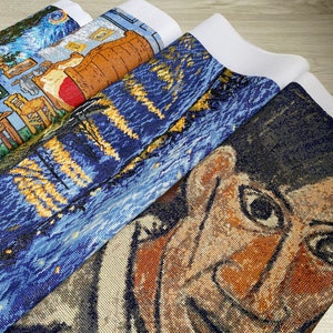 Op de afbeelding: Een stapel van vier onafgewerkte kruissteek-borduurprojecten. Het bovenste project is een blauwe en gele sterrenhemel-sc&egrave;ne. Het tweede project is een blauwe en gele sc&egrave;ne met een gebouw en een boom. Het derde project is een bruine en gele sc&egrave;ne met een vat. Het onderste project is een close-up van een gezicht met bruine huid en donker haar.