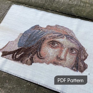 Puede incluir: Un patrón de punto de cruz de la cara de una mujer con un pañuelo azul. El patrón está en tela Aida blanca y el texto "PDF Pattern" es visible en la parte inferior de la imagen.