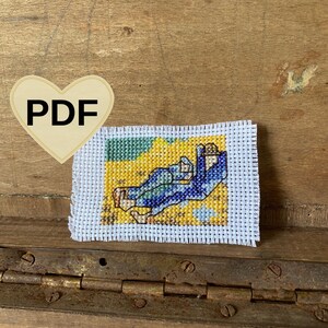 May include: A cross-stitch pattern of two people in blue clothing lying on a yellow beach with a blue sky and white clouds.