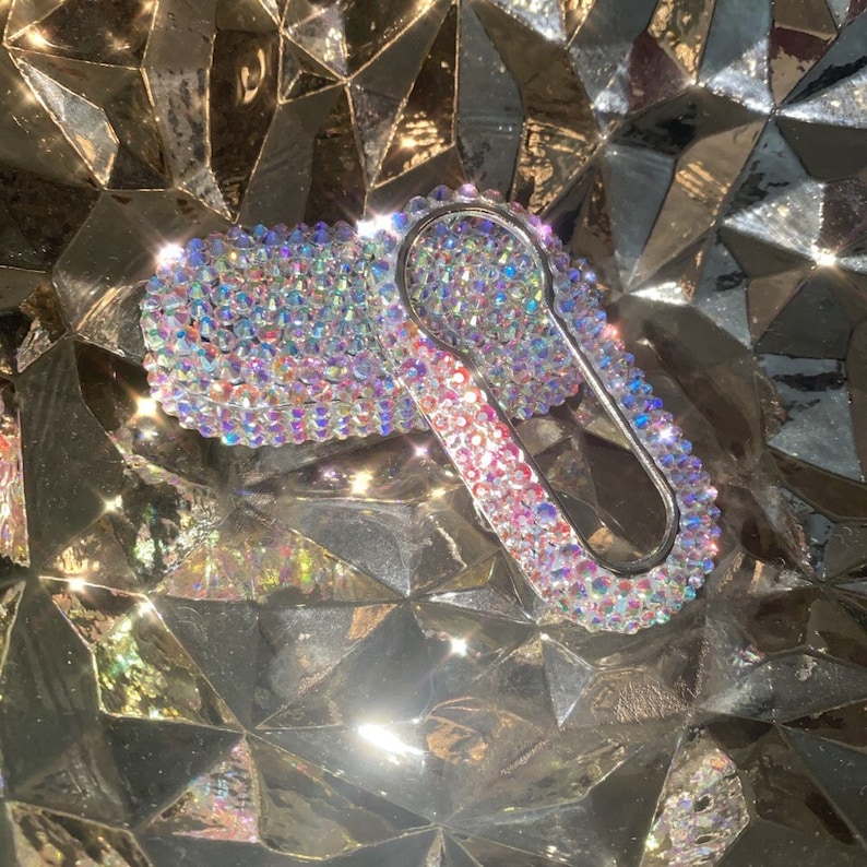 May include: A silver key chain with a clear and iridescent crystal design. The key chain is shaped like a car key and has a small loop at the top for attaching to a key ring.