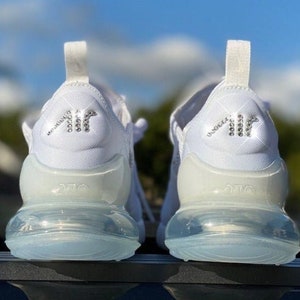May include: A pair of white trainers with a clear air bubble sole. The back of the trainers have a rhinestone "AIR" logo.