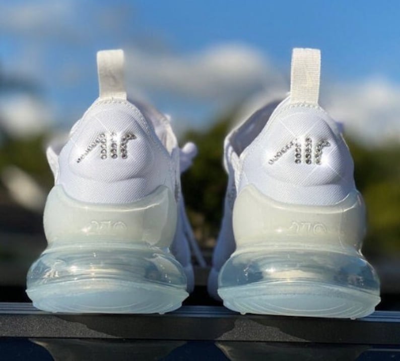 May include: A pair of white trainers with a clear air bubble sole. The back of the trainers have a rhinestone "AIR" logo.