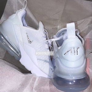 May include: White Nike Air Max 270 trainers with a crystal-encrusted swoosh logo and "Air" lettering. The shoes have a white mesh upper and a clear outsole. #crystalella