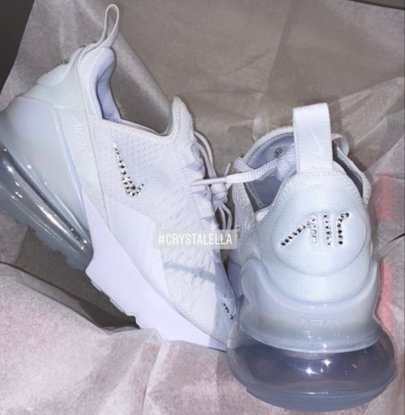 May include: White Nike Air Max 270 trainers with a crystal-encrusted swoosh logo and "Air" lettering. The shoes have a white mesh upper and a clear outsole. #crystalella