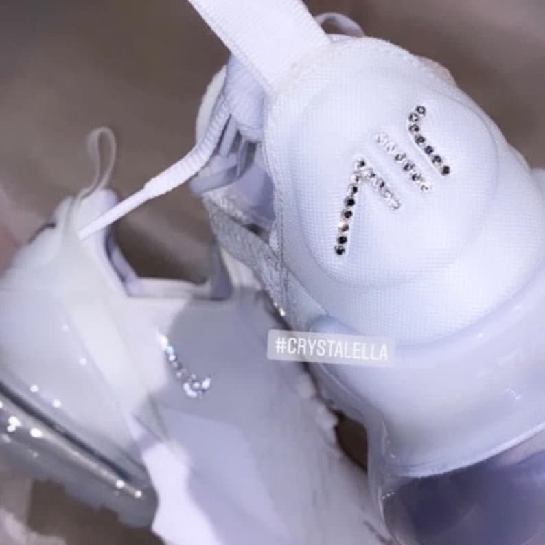 May include: White Nike Air Max 270 trainers with a crystal-embellished "AIR" logo on the back of the shoe. The hashtag #CRYSTALELLA is printed on the side of the shoe.