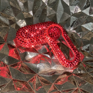 May include: A red key cover with a sparkly, crystal-like finish. The cover is shaped like a key with a keyhole cutout.