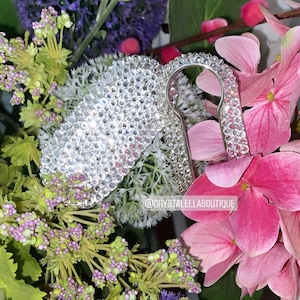 May include: A silver key charm covered in sparkling rhinestones. The charm is shaped like a keyhole and is surrounded by pink flowers.