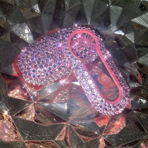 May include: A pink car key cover encrusted with clear rhinestones. The cover is made of a soft, flexible material and has a keyhole cutout.