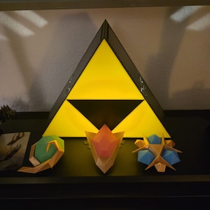 May include: A black and yellow triangular light fixture with a black triangle at the bottom. Below are three geometric shapes in green, orange, and blue. The items are displayed on a black shelf.