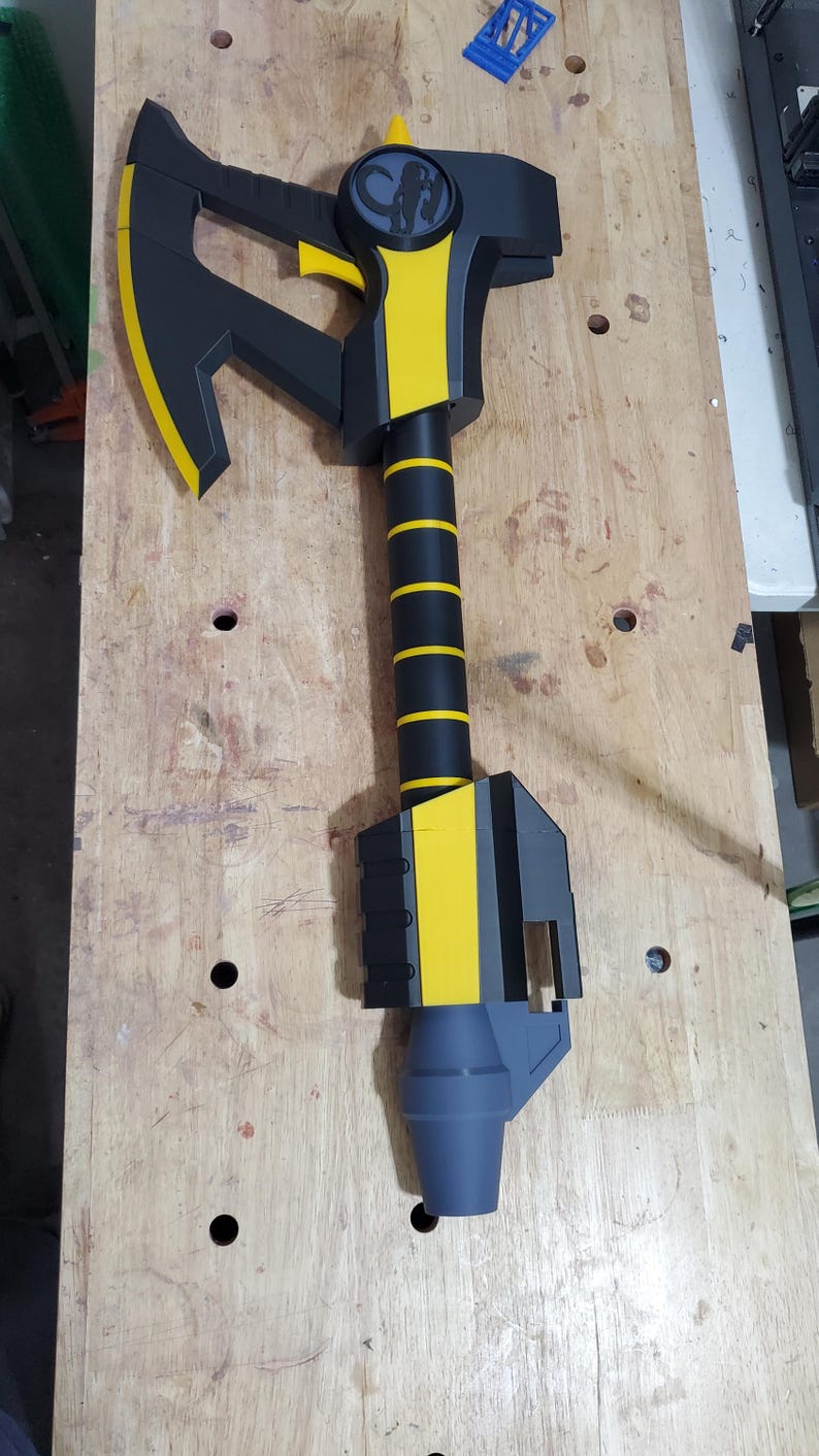 Puede incluir: Un hacha de utiler&iacute;a negra y amarilla con un mango gris y un logotipo en blanco y negro de una criatura en la parte superior de la cabeza del hacha.