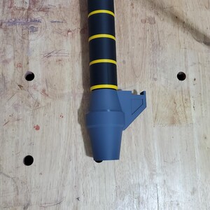 Puede incluir: Un mango de espada negro y amarillo con una punta de pl&aacute;stico gris. El mango tiene un agarre texturizado y un dise&ntilde;o a rayas negro y amarillo.