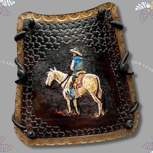May include: A dark brown leather arm guard featuring a stamped geometric pattern and a hand-painted scene of a cowboy riding a light-colored horse. The guard has a tan border with a repeating circular design and black lacing along the sides.